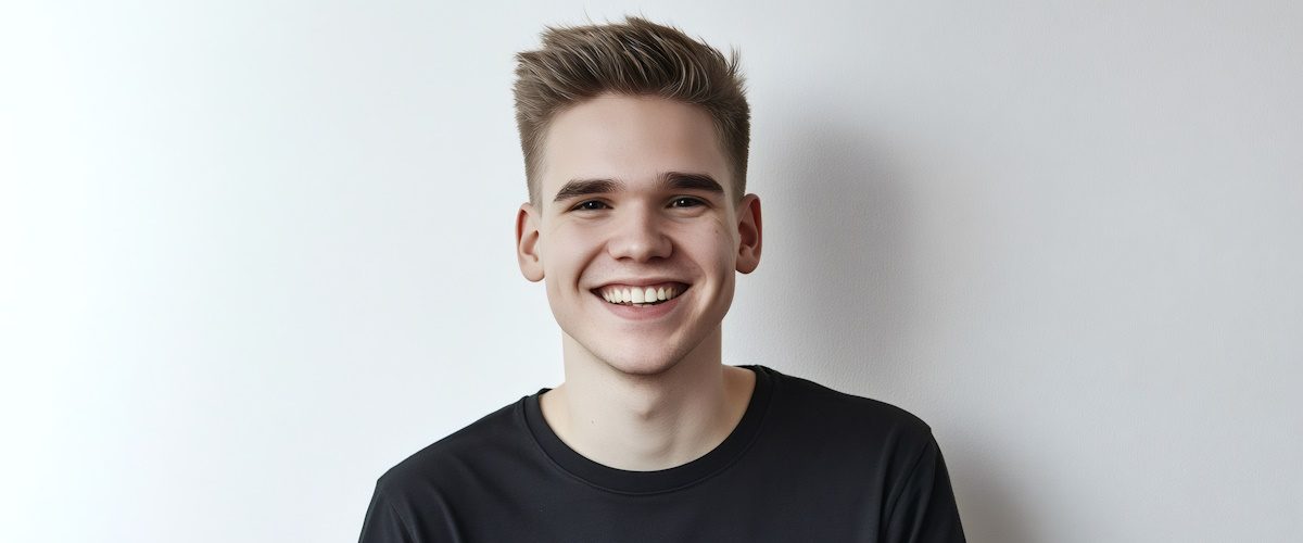 AdobeStock_1157896900 Cheerful young man smiling confidently while wearing a black t shirt against a clean white background, radiating joy and positivity
